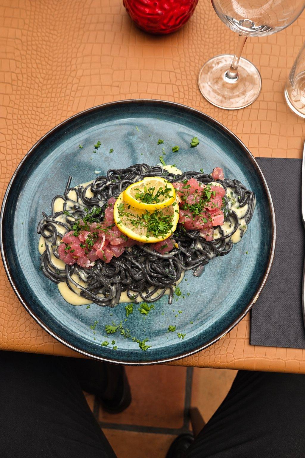 Tagliolini noirs, tartare et citron dans une assiette bleue